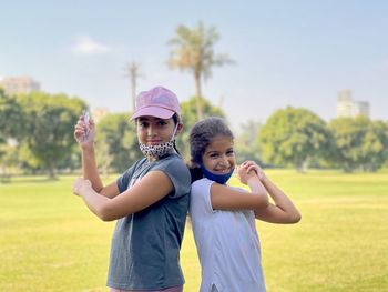 Portrait of two smiling young girls with arms raised standing on field