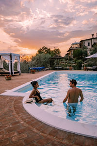 Couple at swimming pool against sky during sunset