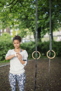 Woman using smart watch standing against gymnastic rings in park