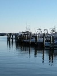 Boats moored at harbor against clear blue sky
