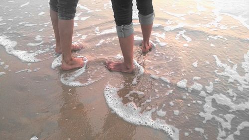 Low section of man standing on wet sand at beach