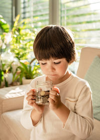 Happy little child holding glass jar full of coins. kid counting money saving from change learning