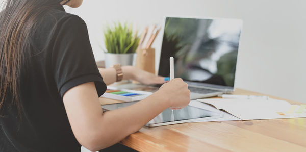 Midsection of woman using mobile phone while sitting on table