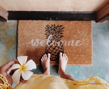 Low section of woman holding frangipani by welcome sign doormat