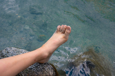 Cropped image of person leg on rock at sea