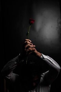 Man with arms raised holding red flower against black background