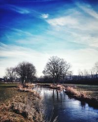 Bare trees by lake against sky