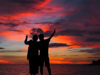 Silhouette couple standing on beach against orange sky