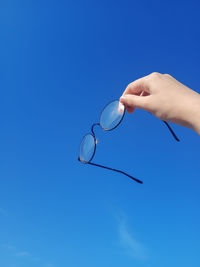 Transparent glasses in a black frame, in his hand, raised up against the blue sky