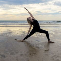 Woman with arms raised on beach against sky during sunset