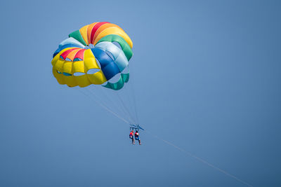 Low angle view of people paragliding against sky