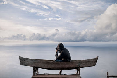 Rear view of woman sitting on boat on lake against sky