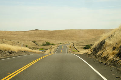 Empty road amidst landscape against sky