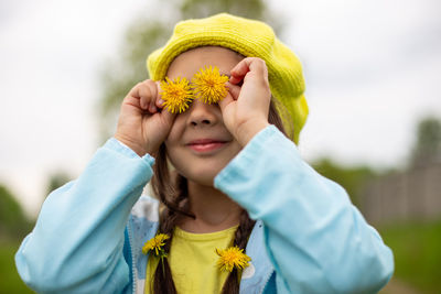 Portrait of a funny charming little girl with two yellow dandelion flowers near her eyes  in spring