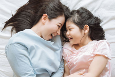 Directly above shot of smiling woman relaxing with daughter on bed at home