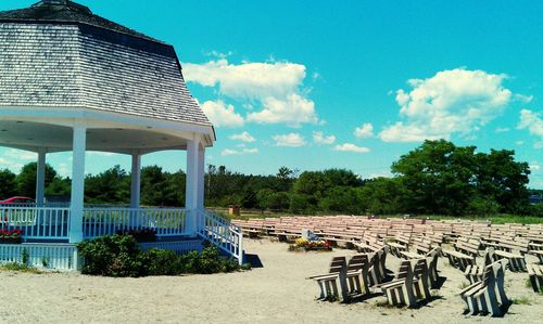 Empty chairs by trees against sky