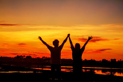 Silhouette people with arms raised against orange sky