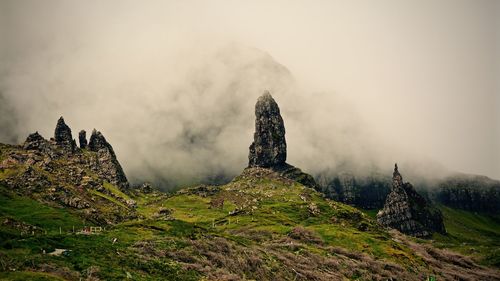 Rock formations on field against sky during foggy weather