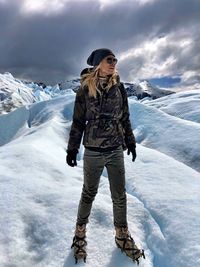 Woman standing on snowcapped mountain against cloudy sky