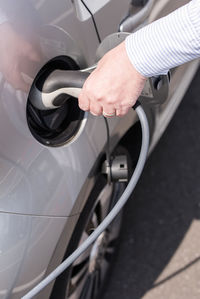 Cropped hand of man charging car at station 