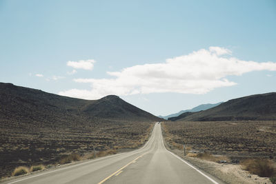 Empty road leading towards mountains against sky