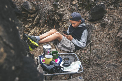 Full length of boy using phone while relaxing on chair at forest