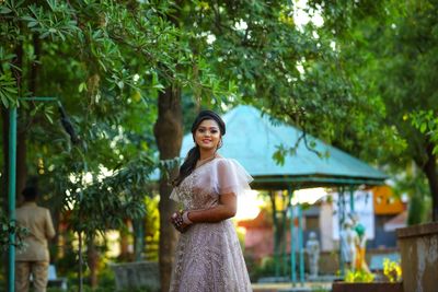 Portrait of smiling young woman standing against trees