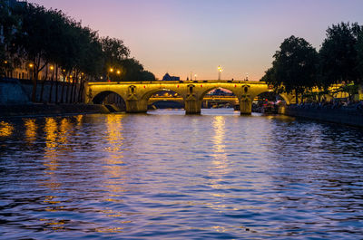 Bridge over river in city against sky at sunset