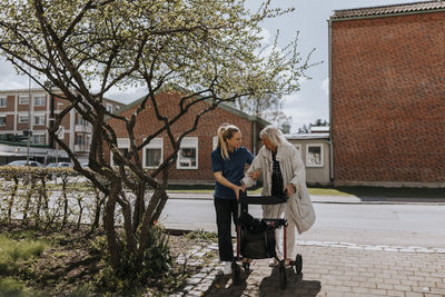 Female caregiver assisting senior woman with walker on footpath