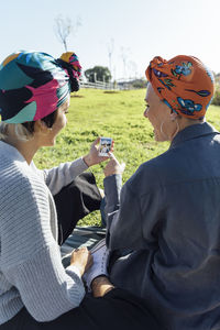 Friends wearing turban looking at instant photograph while sitting at park
