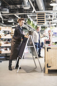 Owner adjusting blackboard while customer shopping in supermarket