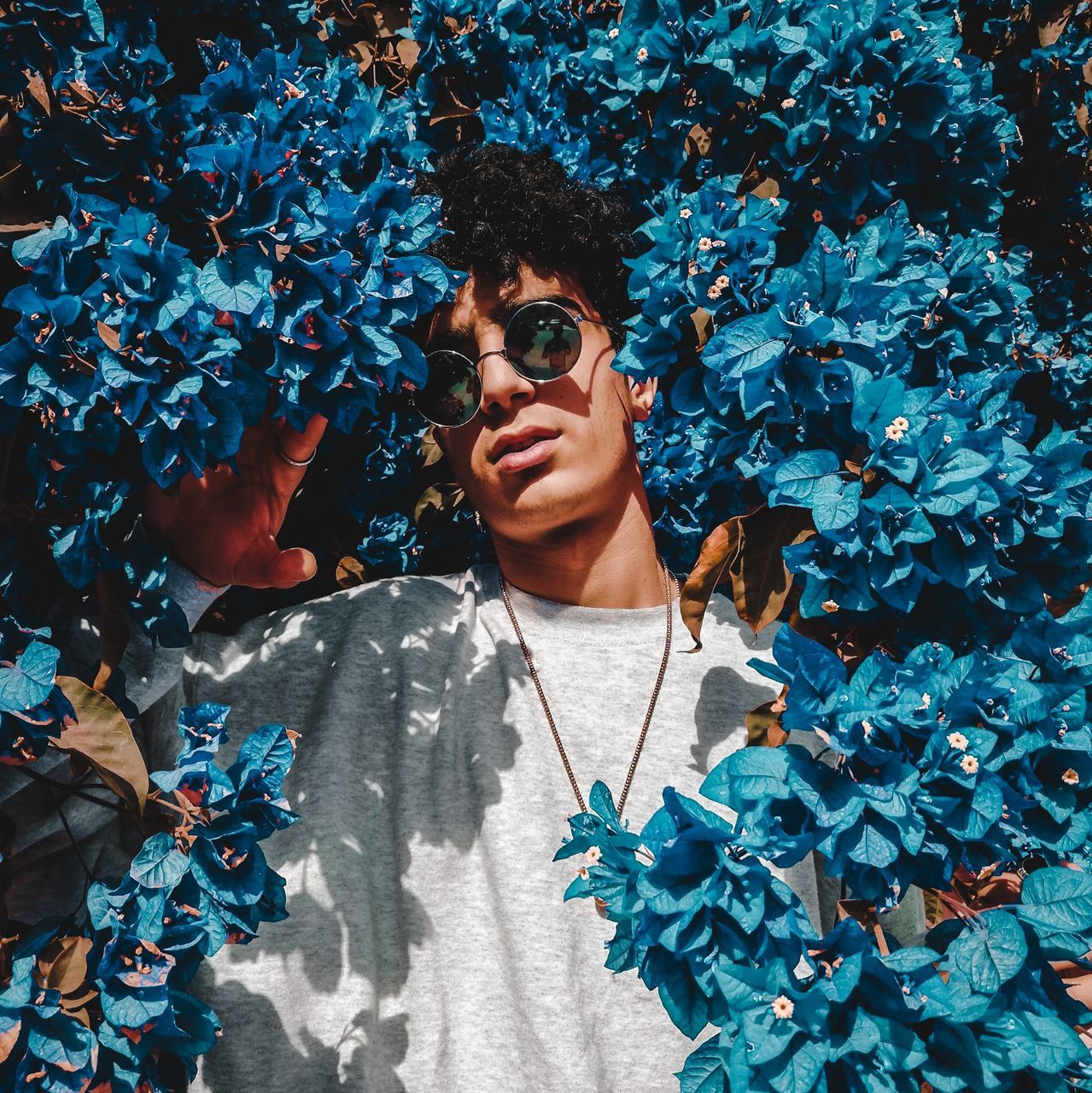 one person, real people, front view, portrait, leisure activity, plant, leaf, lifestyles, looking at camera, plant part, nature, young adult, day, glasses, flower, flowering plant, standing, casual clothing, outdoors, teenager, leaves, hairstyle, teenage boys