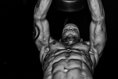 Low angle view of shirtless man exercising against black background