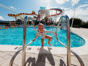 Front view of child exiting swimming pool with bright blue skies