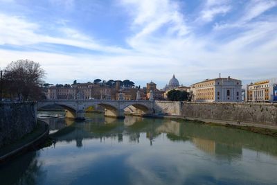 Bridge over river in city against cloudy sky