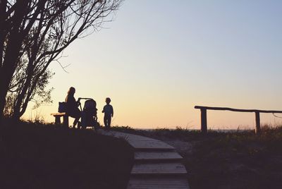 Silhouette people sitting on road against sky during sunset