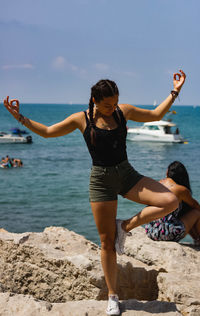 Young woman enjoying on rock at beach against sky