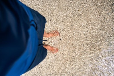 Low section of man standing on sand at beach
