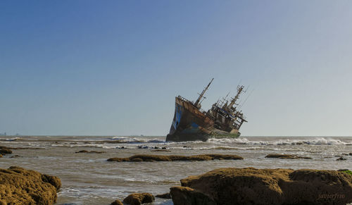 Abandoned ship in sea against clear sky