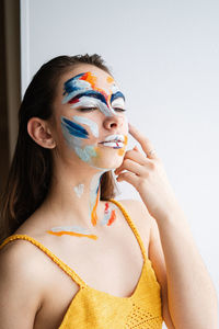 Close-up of young woman with face paint against wall at home
