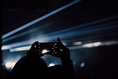 Silhouette person photographing through mobile phone at music concert