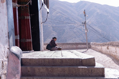 Side view of man sitting on sidewalk against mountain range