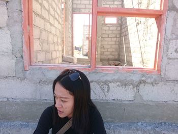 Portrait of young woman against window on wall