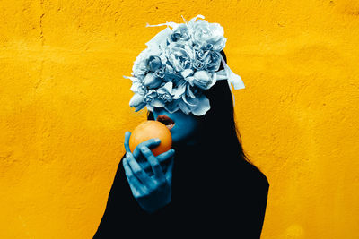 Midsection of person holding umbrella against yellow wall