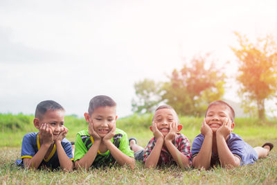 Portrait of happy friends sitting on grass against sky