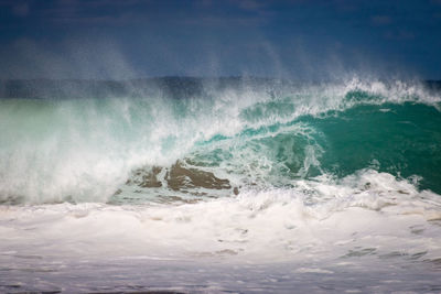 Waves rushing towards shore against sky