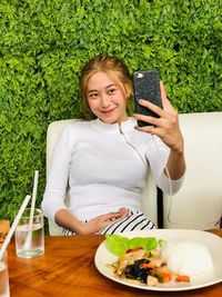 Smiling young woman taking selfie at sidewalk cafe