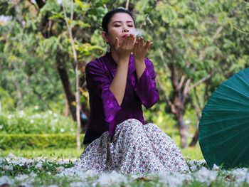 Woman blowing flower while sitting on field