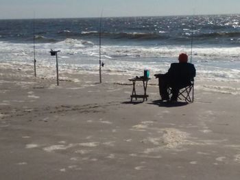 Silhouette man sitting on beach against sky