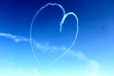 Low angle view of heart shape made of vapor trail against blue sky